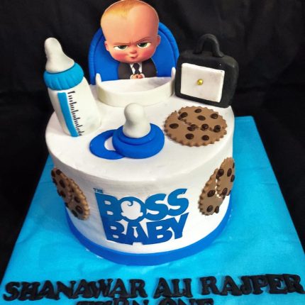 A custom-made Boss Baby-themed cake featuring a figure of Boss Baby, a bottle, cookies, and a briefcase, with a personalized name at the base.