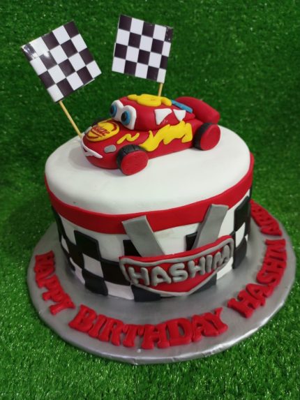 Race car-themed birthday cake with checkered flags, red racing car topper, and personalized name for Hashim