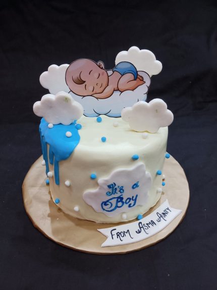 A baby shower cake for karachittes with a sleeping baby on top, surrounded by clouds, and the text 'It's a Boy' with a personalized message at the base.