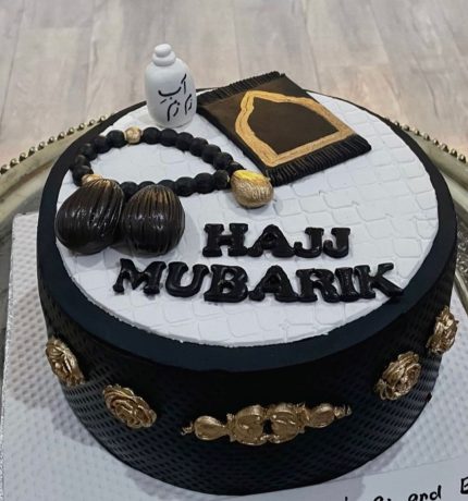 Black and white Hajj Mubarak cake with prayer beads, Kaaba replica, and golden accents