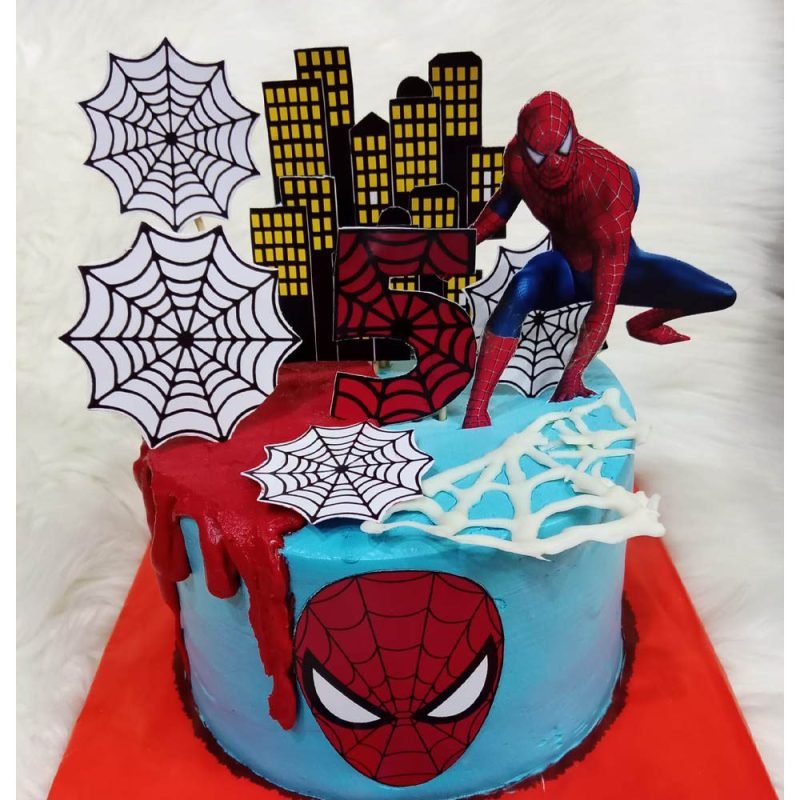 Custom Spider-Man cake featuring web decorations, cityscape backdrop, and a Spider-Man figurine, created for a 5th birthday celebration in Karachi.