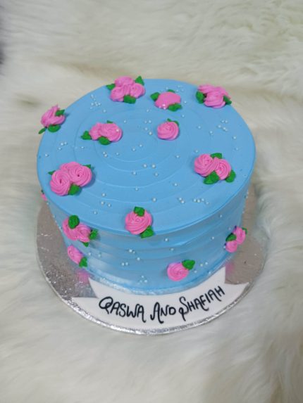 A round blue bento cake decorated with pink flowers and personalized writing on the base.