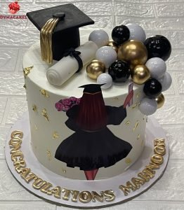 Black and gold graduation cake with edible cap, scroll, gold decorations, and “Congratulations” topper.