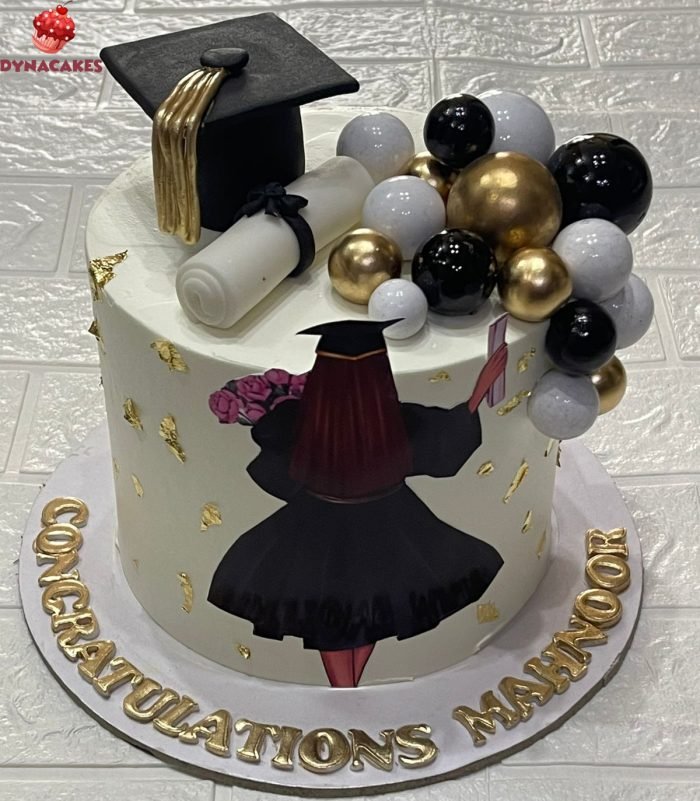 Black and gold graduation cake with edible cap, scroll, gold decorations, and “Congratulations” topper.